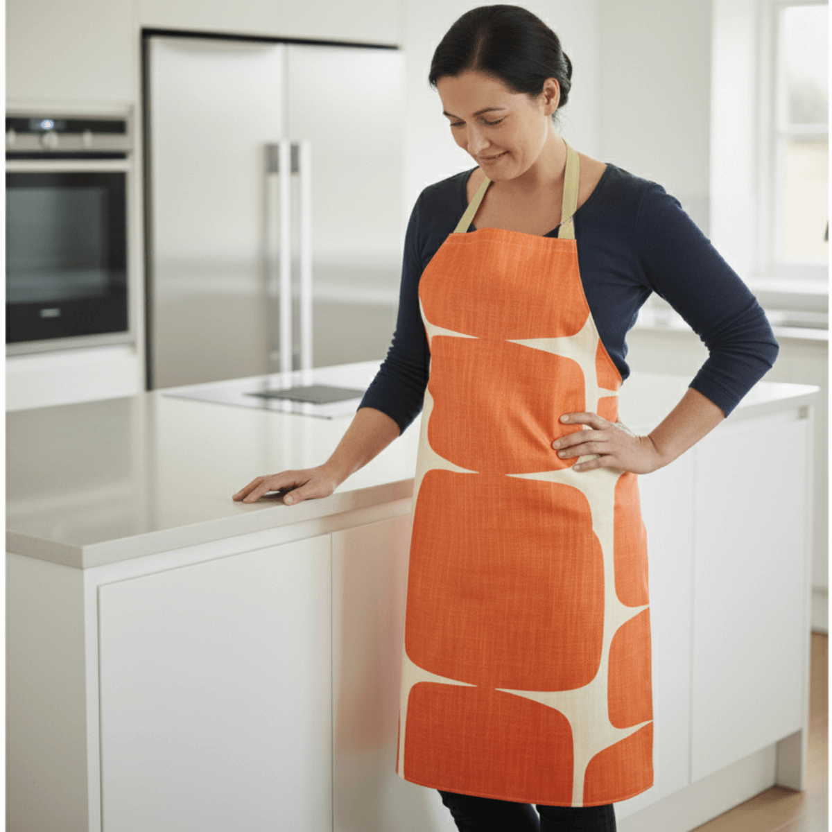 Scion lohko Paprika Oilcloth Apron on. lady in modern kitchen